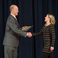 Doctor Potteiger shaking hands with an award recipeint in a black, grey, and white striped sweater dress